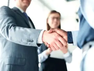 two business people shaking hands in front of a woman.